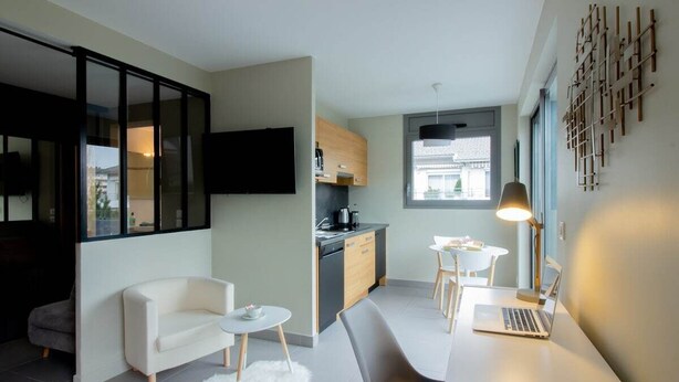 A modern living room with a sofa, a coffee table, and a dining area with a laptop.