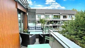 A balcony with a green table and chairs, a wooden wall, and a view of neighboring buildings.