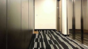 A hallway with metallic lockers, a patterned carpet, and glass doors leading to rooms.