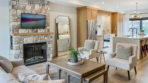 A modern living room with a stone fireplace, a flat-screen TV, and a dining area with a kitchen in the background. - Luxury townhome - Rooftop Patio - Hot Tub (Charlottetown)