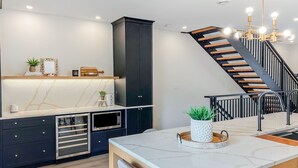 A modern kitchen with dark cabinetry, a marble countertop, and a dining area with a white table and grey chairs. - Luxury townhome - Rooftop Patio - Hot Tub (Charlottetown)