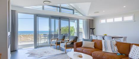 Un salón amplio con un gran ventanal con vistas al mar, un sofá de cuero y una zona de comedor con mesa y sillas.