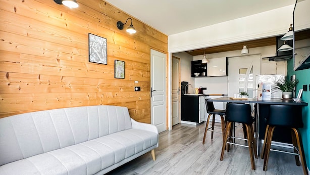 A modern kitchen with wooden walls, a white sofa, and bar stools. - Etoile des neiges 2 min du centre (Annecy)