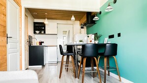 A modern kitchen with a teal accent wall, wooden flooring, and black bar stools. - Etoile des neiges 2 min du centre (Annecy)