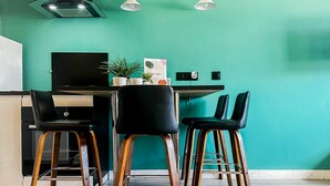 A teal-colored room with a dining table, four black chairs, a kitchen area, and a ceiling light fixture. - Etoile des neiges 2 min du centre (Annecy)
