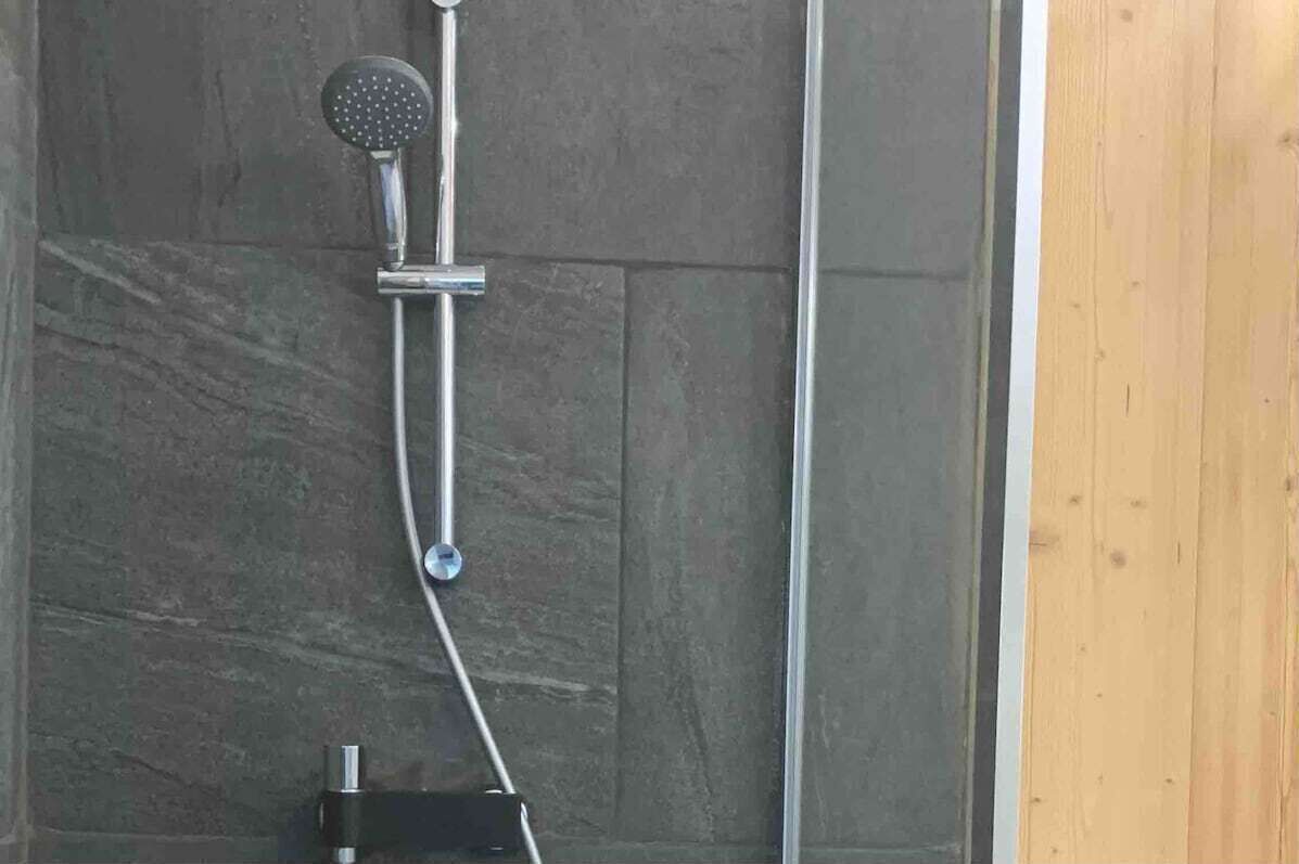 Ducha con cabezal de ducha de mano y panel de control en la pared.