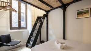 Un dormitorio con cama, una silla, una escalera y una ventana.