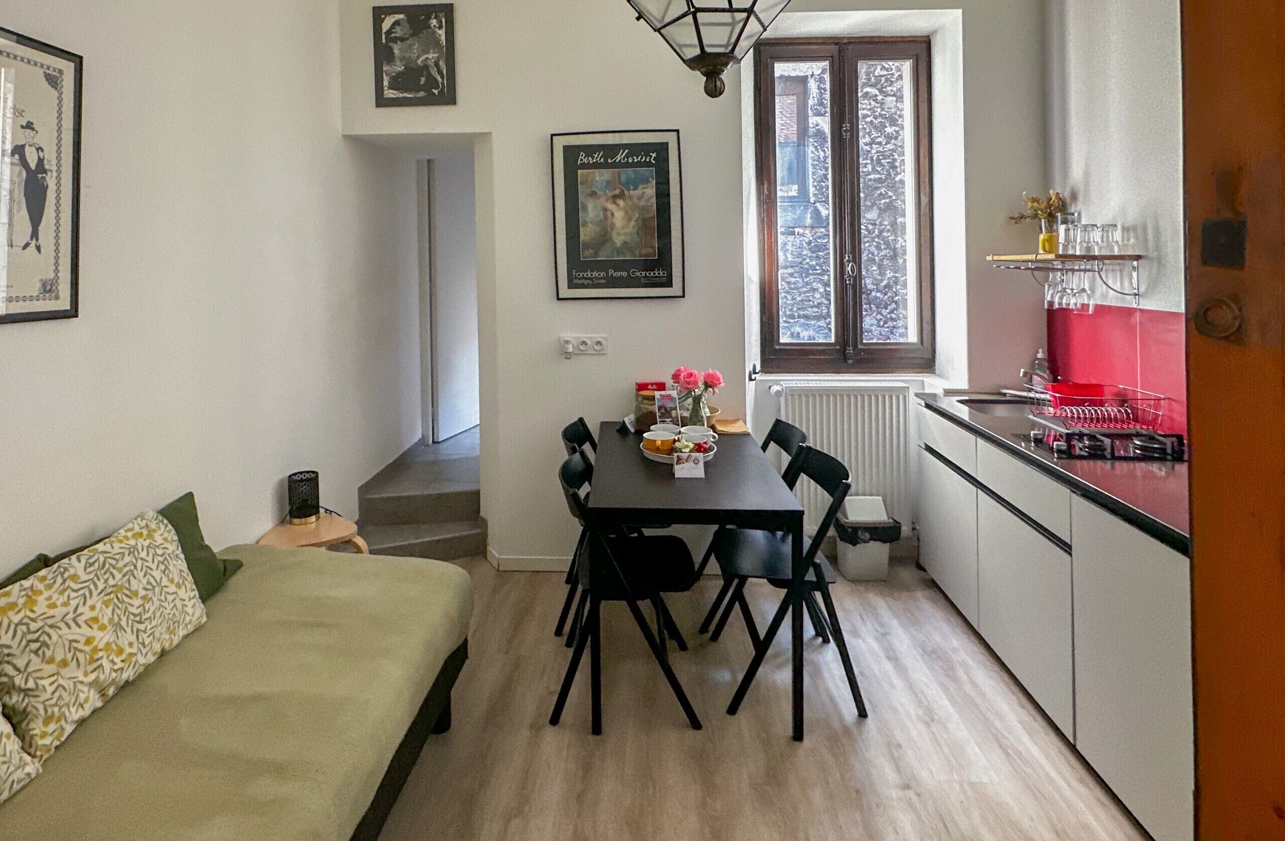Un espacio habitable compacto con una mesa de comedor, sillas, sofá, zona de cocina y ventana con vistas.