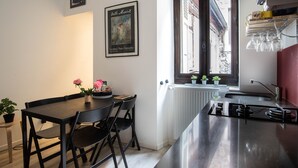 Una cocina moderna con encimera negra, una mesa de comedor con sillas, un ventanal con vistas a un edificio y un radiador.