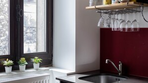 Una cocina con ventana, plantas en macetas, una repisa con tazas y vasos, y un lavamanos.