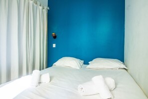 Habitación de hotel con una pared azul de acento, cama con ropa blanca y cortina.