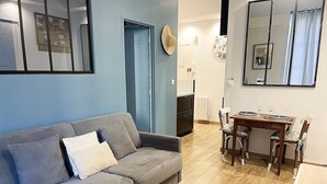Un salon avec un canapé gris, une table à manger avec des chaises et une petite table blanche.
