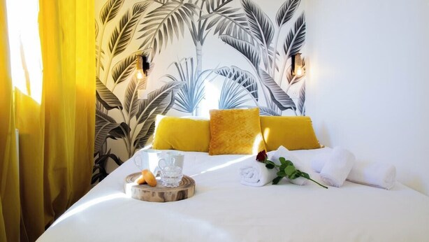 A neatly made bed with yellow pillows, a glass of water, and a tray with a croissant and a flower. - Tahiti Beach 100 m du lac (Annecy)