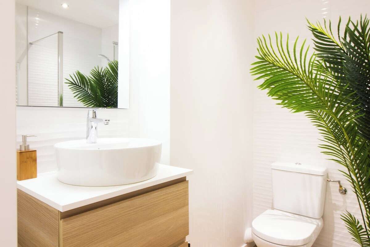 A modern bathroom with a round white sink, wooden vanity, and a toilet.