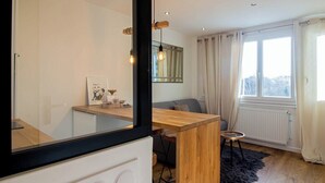 A modern living room with a wooden dining table, a sofa, a large mirror, and a view of the city through a window. - Tahiti Beach 100 m du lac (Annecy)