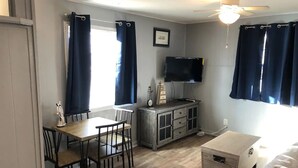 Un espace de vie compact comprenant un coin repas, un téléviseur fixé au mur et un ventilateur de plafond.
