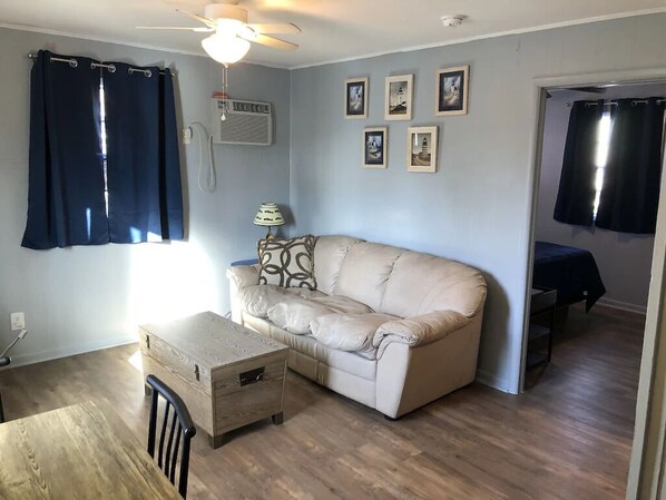 Una sala de estar con un sofá color beige, una mesa de centro de madera, un ventilador de techo y un teléfono montado en la pared.