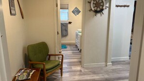 Un couloir avec une chaise verte, une table en bois sur laquelle sont posés des magazines, une décoration représentant un gouvernail de bateau et une pancarte indiquant « Bienvenue ».