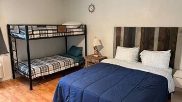 A room with a bunk bed, a single bed, a wooden headboard, a bedside table with a lamp, and a wall clock.