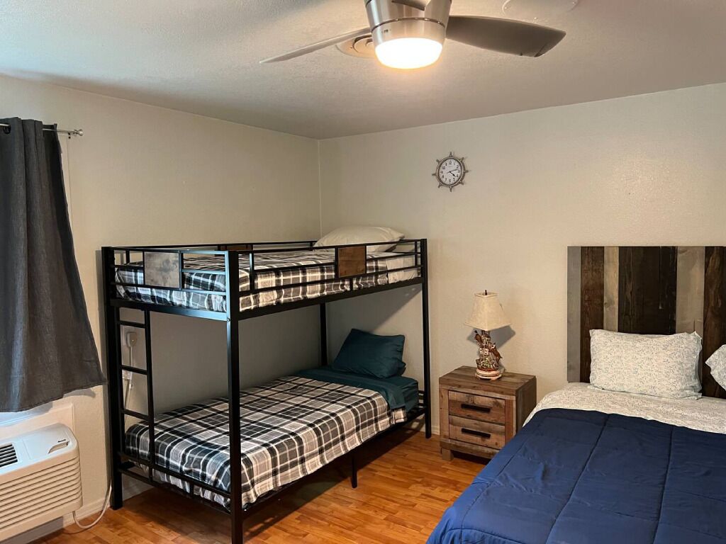 A bunk bed room with a ceiling fan, a bedside table with a lamp, and a clock on the wall.