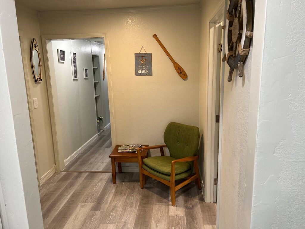 A hallway with a wooden chair and a small table, a mirror, a wall-mounted bat, and a sign reading "LIFE AT THE BEACH".