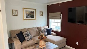 Un salon avec un canapé beige, une table basse en bois et un téléviseur fixé au mur.