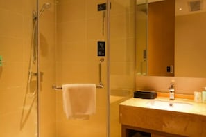 Un baño de hotel con ducha de vidrio, lavamanos con espejo y perchero para toallas.