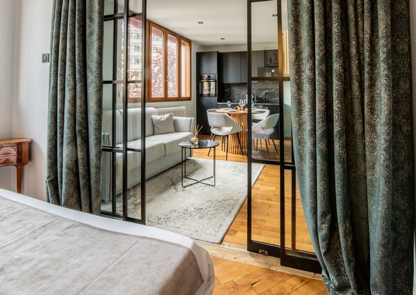Une chambre d’hôtel moderne dotée d’un grand lit, d’un canapé, d’un coin repas avec une table et des chaises, et offrant une vue sur l’extérieur grâce à une paroi vitrée.