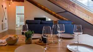 Un comedor con una mesa de madera dispuesta para una comida, un sofá azul al fondo y un techo inclinado con vigas a la vista.