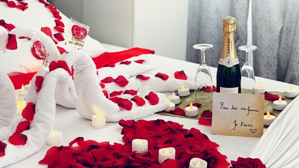 Ambiente romántico con pétalos de rosa, velas, una botella de champán y una nota.