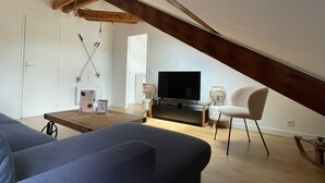 Una sala de estar estilo loft acogedora, con techo inclinado, televisor de pantalla plana, una mesa de centro, un sofá y una silla.