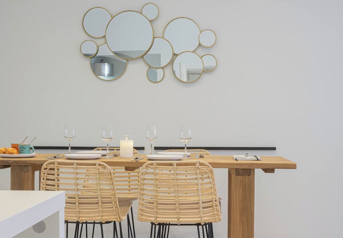 Een eethoek met een houten tafel voor vier personen, twee rieten stoelen en een spiegelopstelling aan de muur.