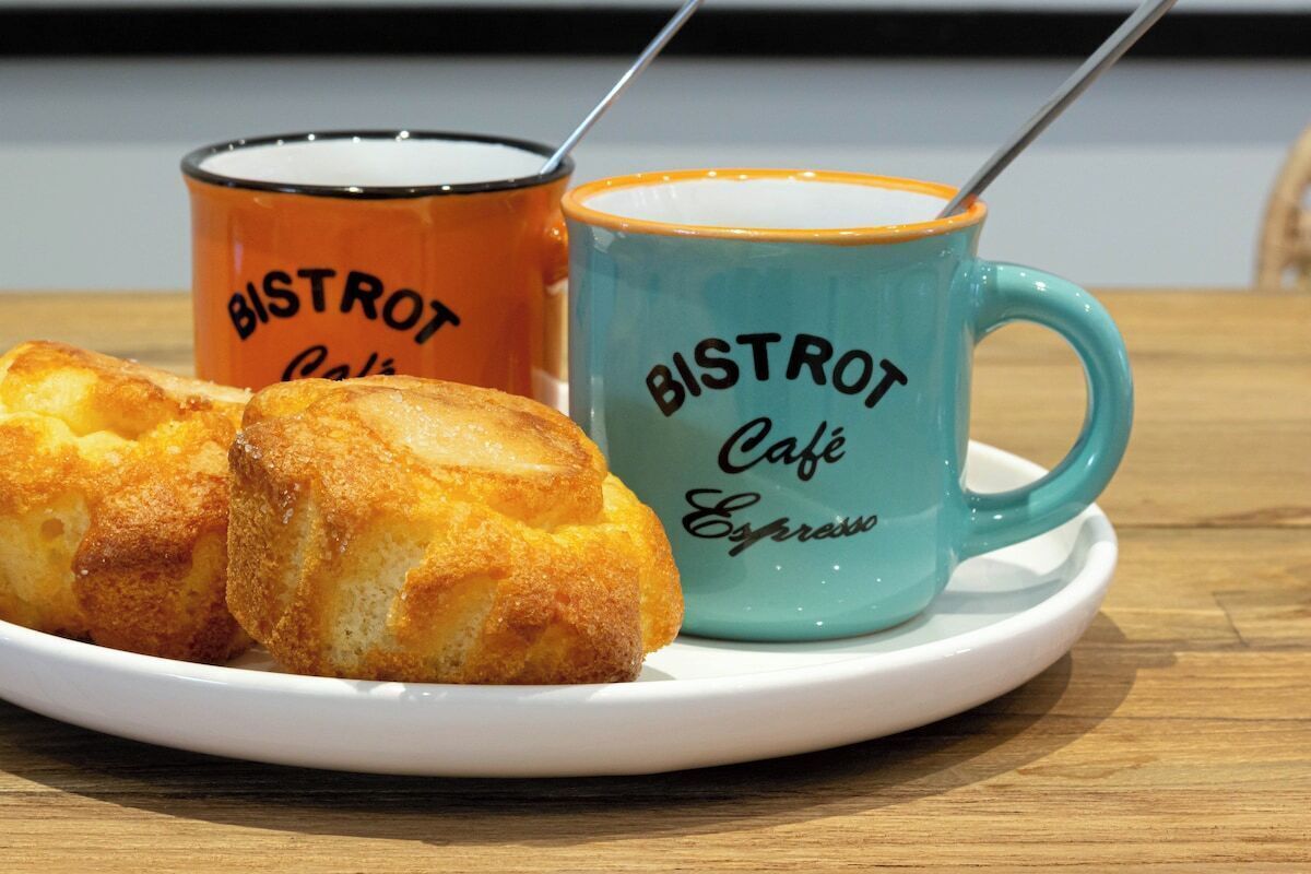 Een bord met gebak en twee mokken met de tekst 'BISTROT Café Espresso' op een houten tafel.