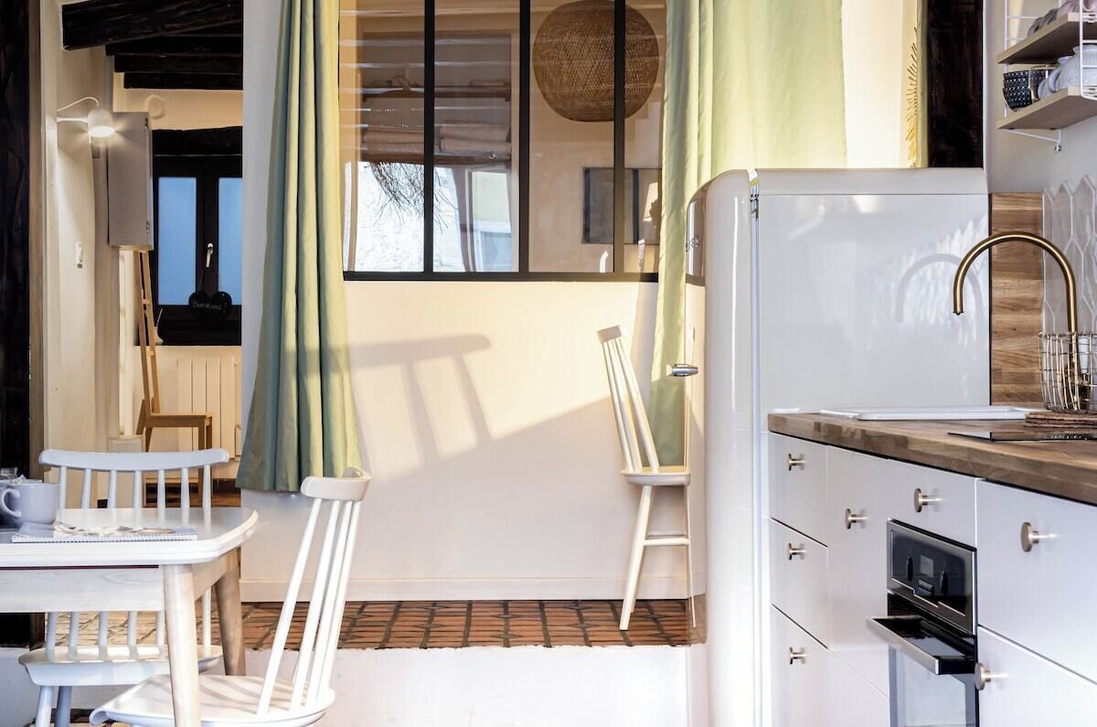 A compact kitchen with a white refrigerator, a wooden countertop, and a built-in oven. There is a small dining area with a white table and two chairs.