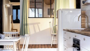 Cocina compacta con refrigerador blanco, cubierta de madera y horno empotrado. Cuenta con un pequeño comedor con mesa blanca y dos sillas.