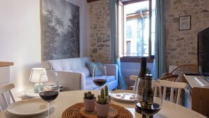 Un comedor con una mesa dispuesta para dos personas, un cuadro en la pared y un muro de piedra al fondo.