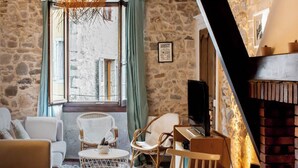 Un salón acogedor con paredes de piedra, una chimenea y un amplio ventanal con cortinas.