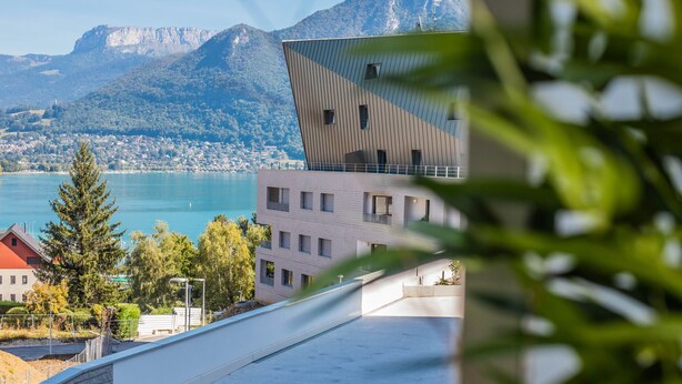 En modern byggnad med en unik, kantig design, med utsikt över en sjö och berg.