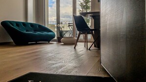 En modern inredning med en turkos soffa, en svart stol och ett trägolv. En dörrmatta med texten ”L’élégant” syns.