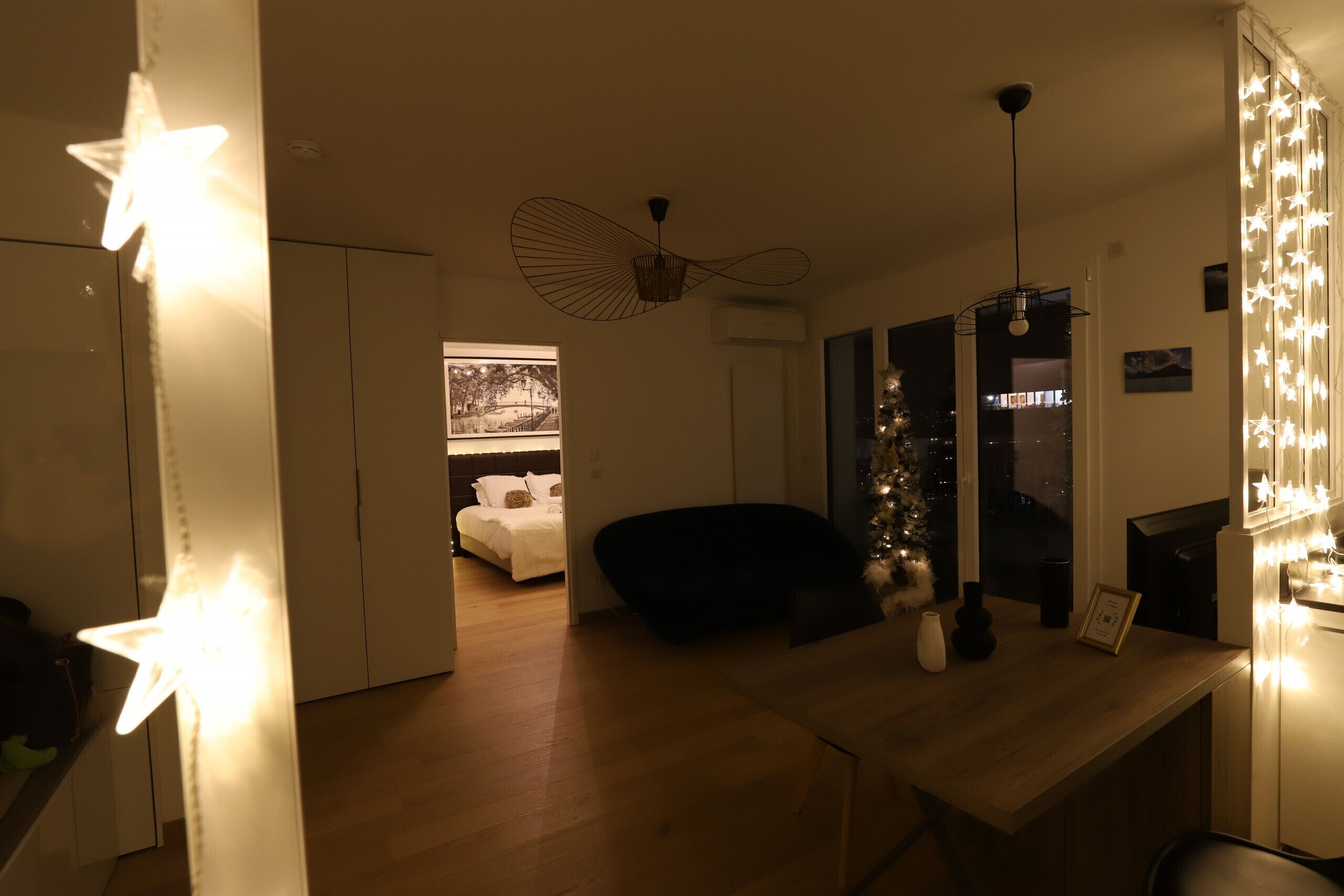 A modern living room with a wooden floor, a black sofa, a dining table, and a Christmas tree.