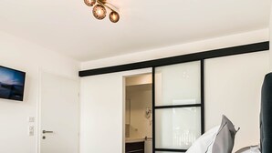 Ett modernt hotellrum med en stor säng, en platt-TV som är monterad på väggen och en skjutdörr som leder in till badrummet.