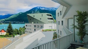 En modern byggnad med ett unikt, triangulärt tak, en balkong med räcke och utsikt över ett bergigt landskap och en sjö eller ett annat vattendrag.