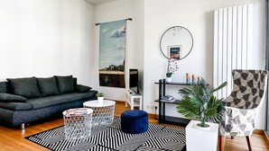 A modern living room with a dark grey sofa, a round coffee table, a blue ottoman, and a patterned rug. - Garden plazza T2 standing parking (Annecy)