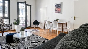 A modern living room with a sofa, a coffee table, and a dining area with chairs and a table. - Garden plazza T2 standing parking (Annecy)