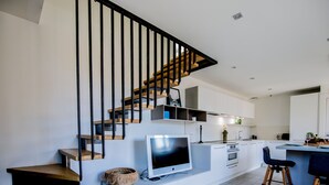 A modern kitchen with a built-in TV, wooden staircase, and a dining area with bar stools. - Duplex d'Albigny 3 minutes du lac (Annecy)