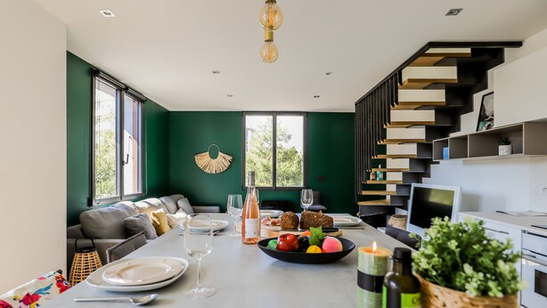 A modern kitchen with a dining area, featuring a staircase, built-in shelves, and a large window. - Duplex d'Albigny 3 minutes du lac (Annecy)