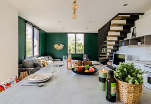A modern kitchen with a dining area, featuring a staircase, built-in shelves, and a large window. - Duplex d'Albigny 3 minutes du lac (Annecy)