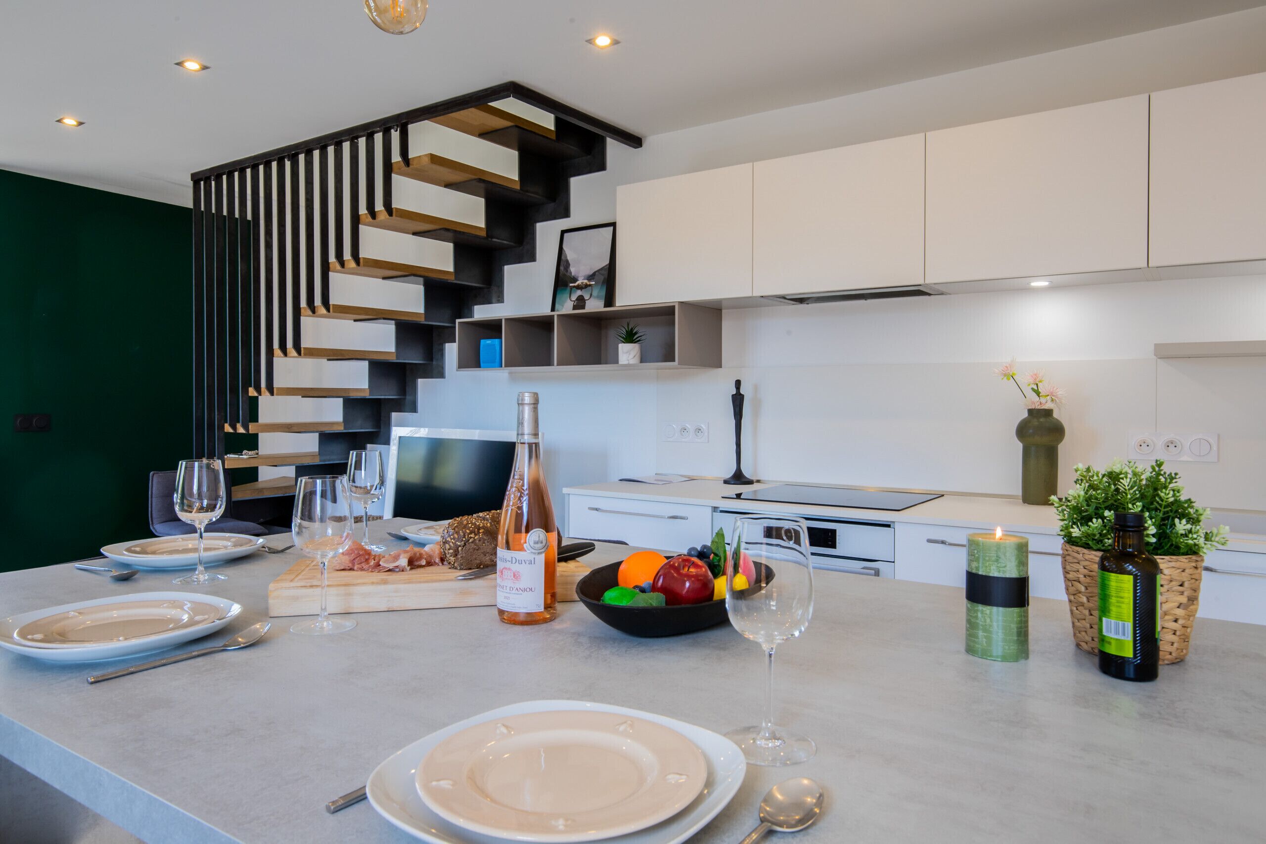 Une cuisine moderne dotée d’un escalier intégré, d’un coin repas avec des assiettes et des verres, et d’un panier de fruits.