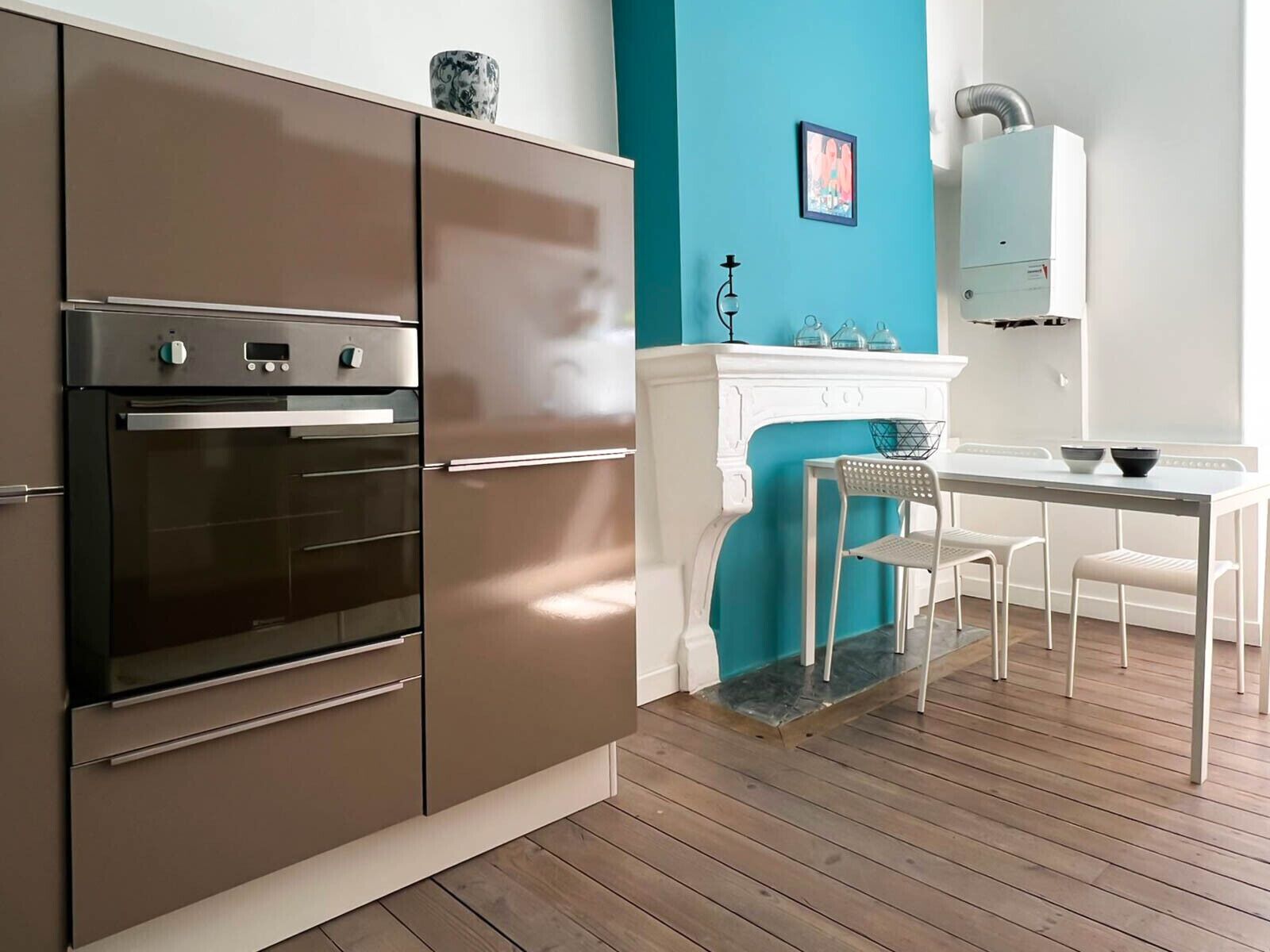 Une cuisine moderne dotée d’un four encastré, d’une table à manger blanche avec des chaises, et d’un mur d’accent de couleur turquoise.