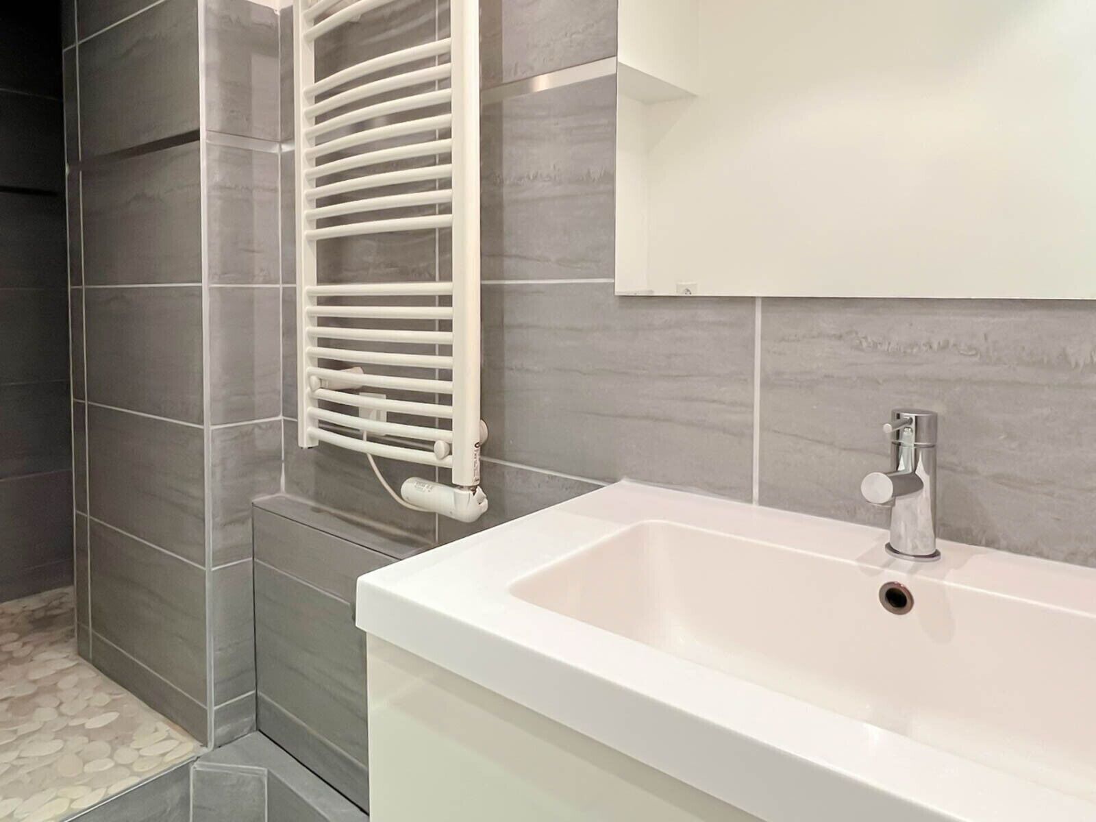 A modern bathroom with a white sink, a towel rack, and grey tiled walls.